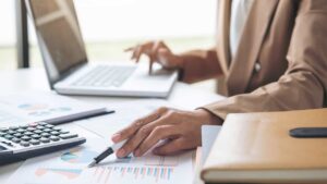 A photo of a person at a desktop with a laptop, calculator and business report