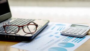 A laptop, pair of glasses, printed business reports and a calculator