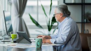Older man in blue shirt typing on a laptop