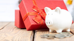 A piggy bank, coins, and a red gift box sit on a wood table.