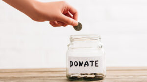 A hand donating a coin to a donation jar.