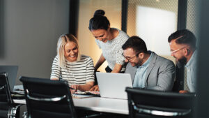 Group of four businesspeople surrounding a table with a laptop.
