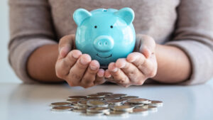 Hands holding a blue piggy bank over coins.