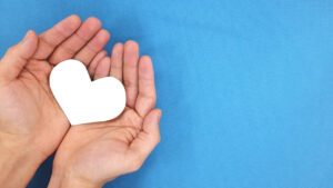Hands open, holding a white heart on a blue background.