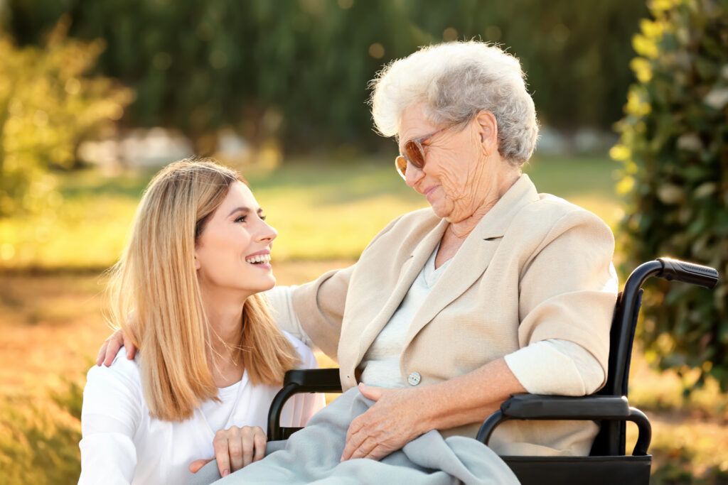 An elderly woman in a wheelchair and a younger woman look at each other.