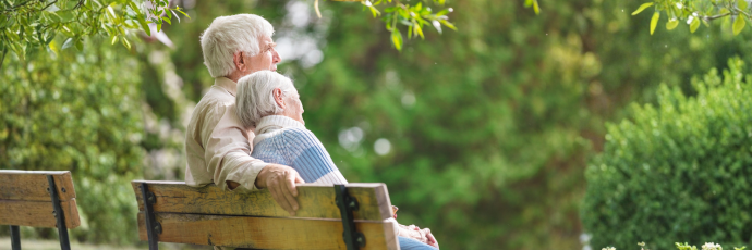 An elderly couple rests on a park bench.