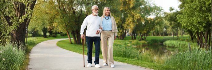 An elderly man and woman walk on a park path.